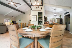 A dining area with a round wooden table set for four, surrounded by wicker chairs with green cushions.