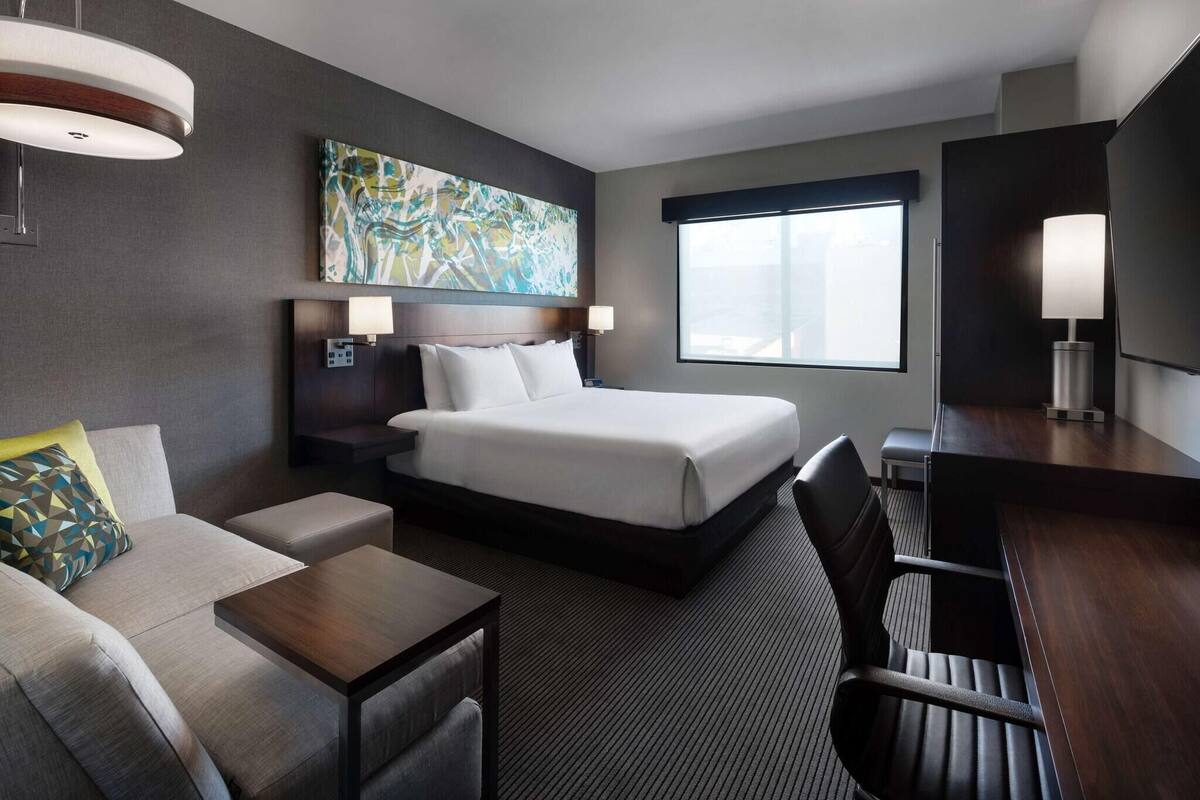 A hotel room with a bed, a desk, a sofa, a lamp, and a painting on the wall.