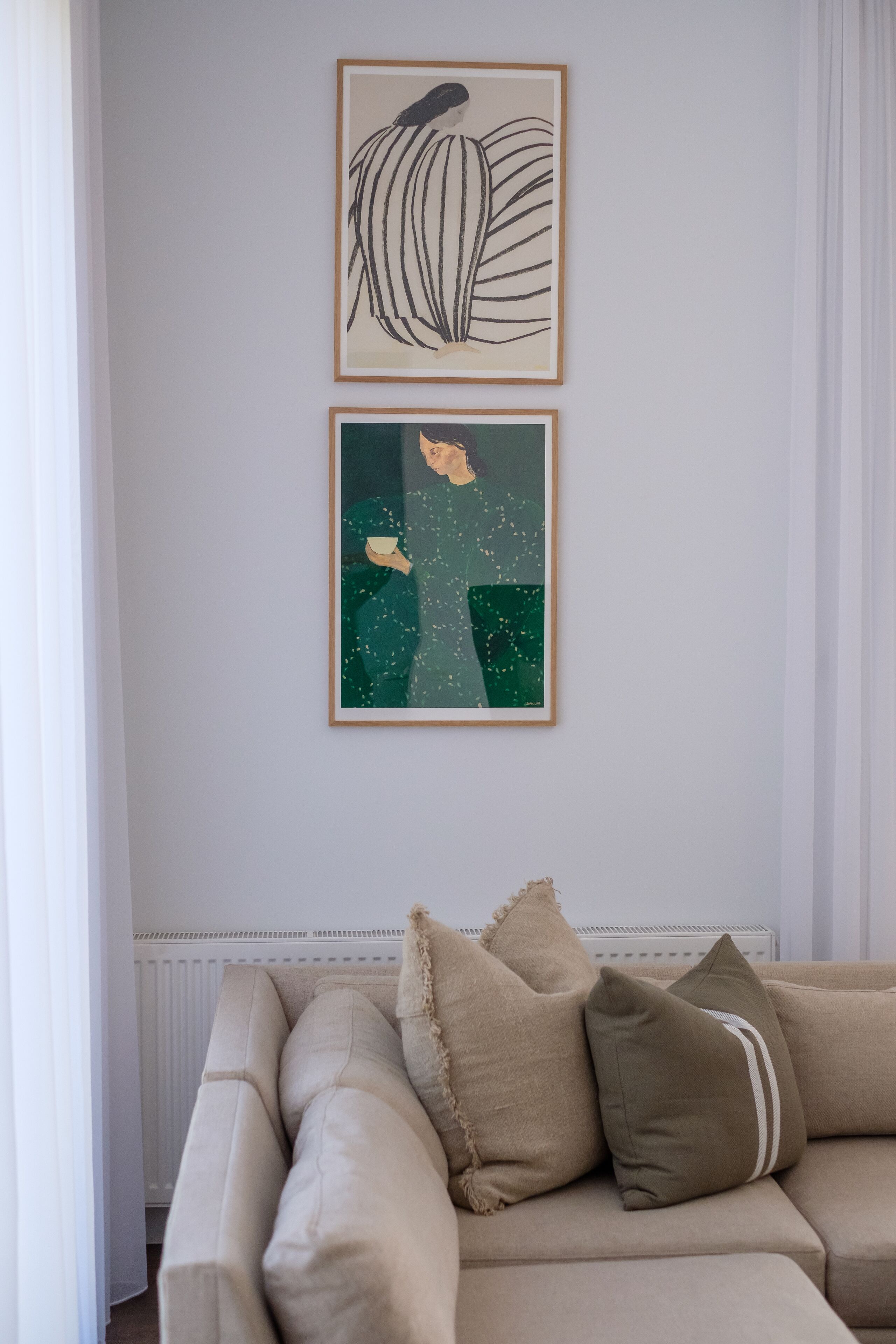 Una sala de estar con un sofá color beige, dos obras de arte enmarcadas en la pared y un radiador blanco debajo.