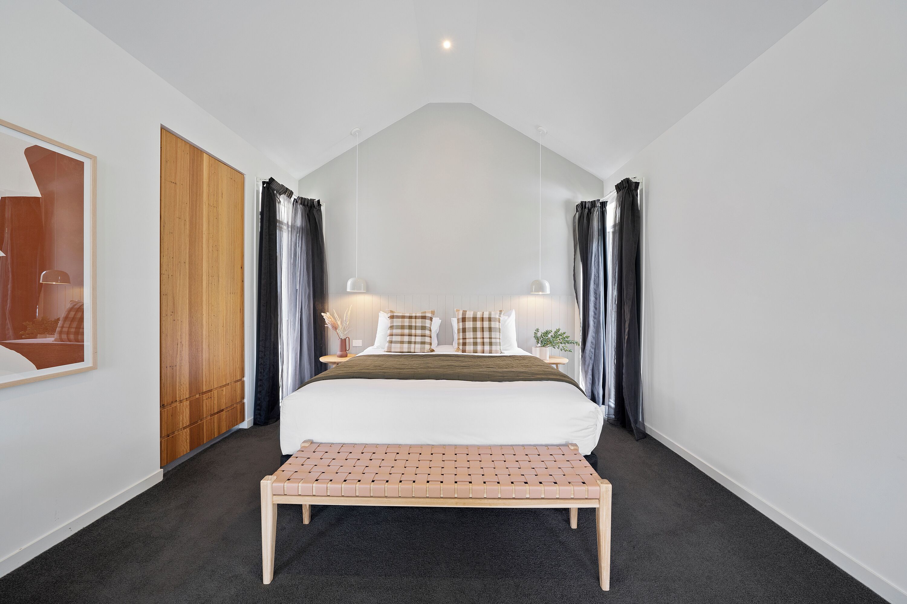 A bedroom with a bed, bench, curtains, and a wooden wardrobe.