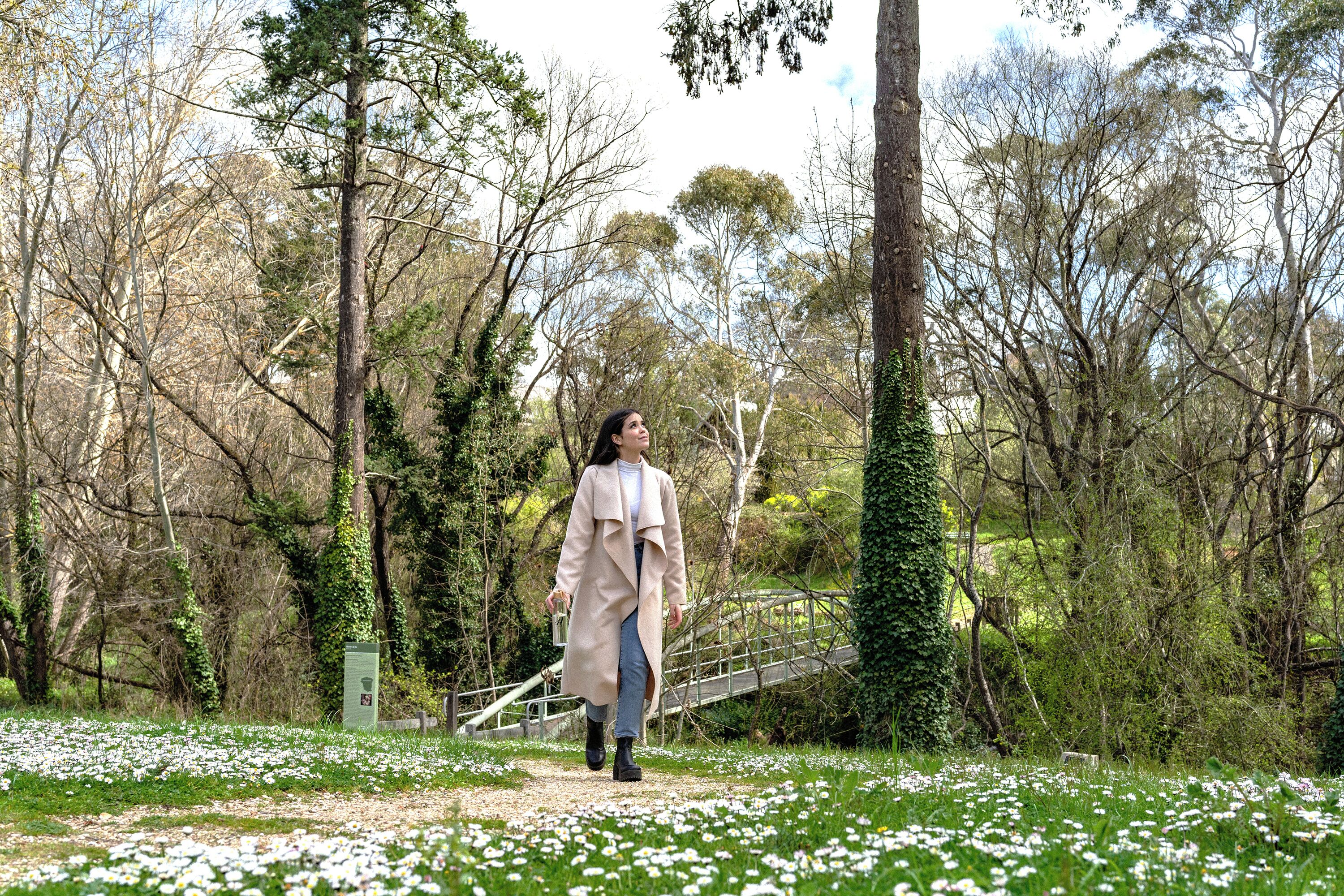 Una mujer caminando por un sendero rodeado de árboles y flores blancas.