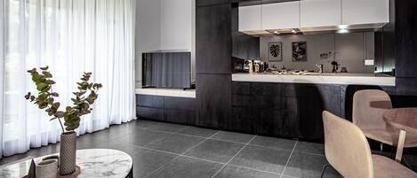 A modern kitchen with dark cabinetry, a white countertop, and a large window with sheer curtains.