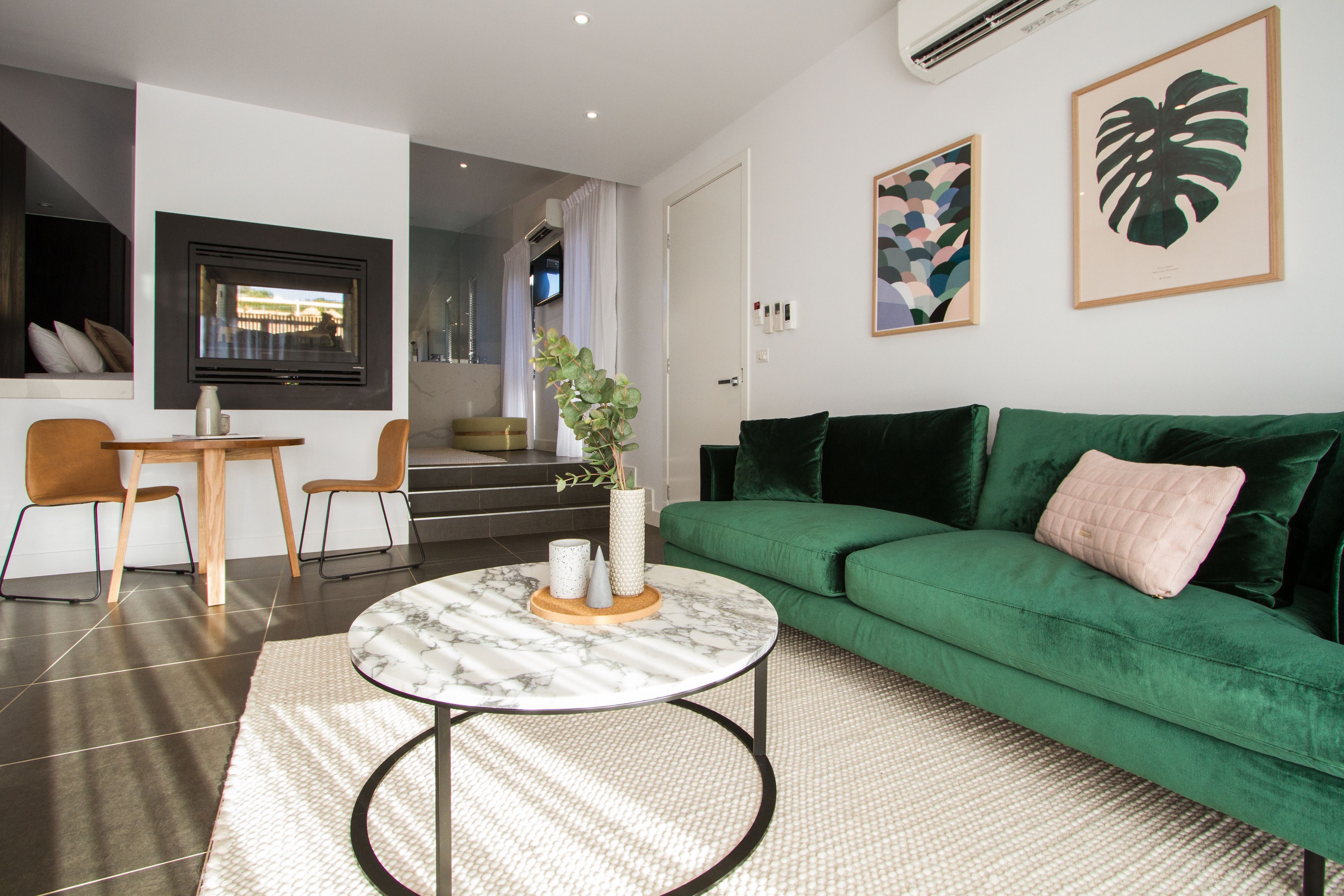Un salon moderne avec un canapé vert, une table basse ronde et un téléviseur fixé au mur.