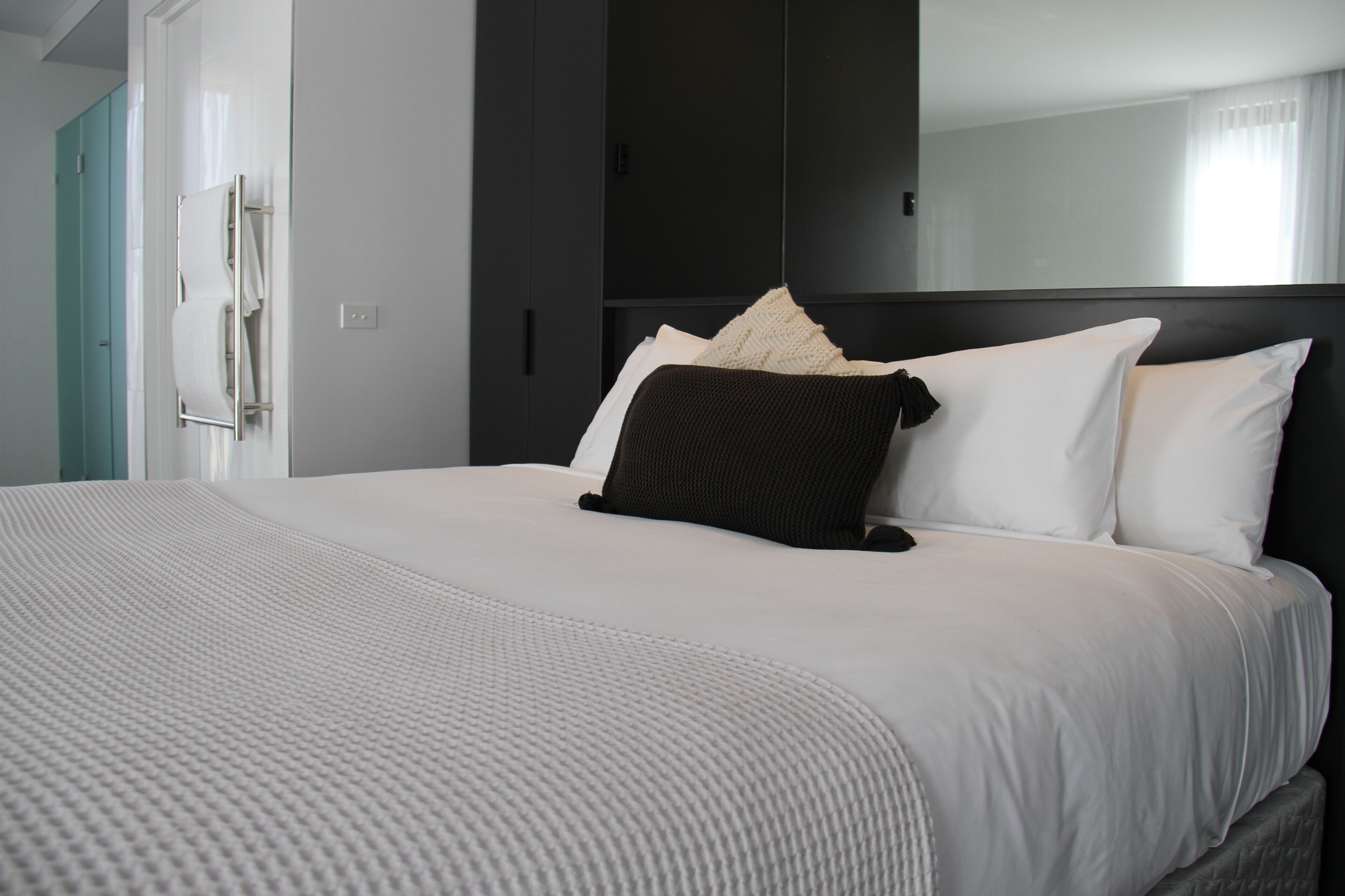 A modern hotel room with a large bed, a dark headboard, and a wardrobe.