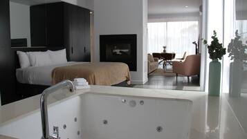 A modern hotel room with a large bed, a bathtub, a seating area with a table and chairs, and a large window.