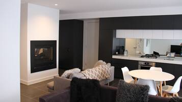 Een moderne woonkamer met een open haard, een bank met een decoratief plaid en een eethoek met een witte tafel en stoelen.