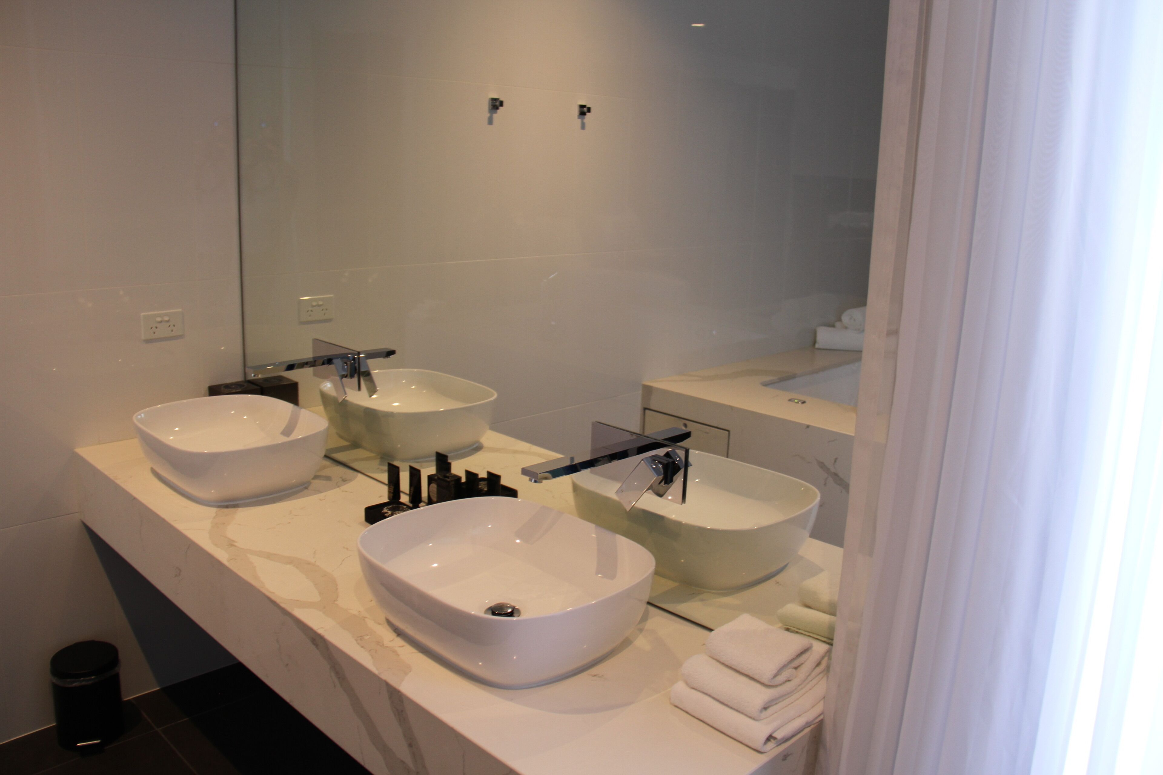 A modern bathroom with two large, white vessel sinks, a glass shower enclosure, and a mirror above the sinks.