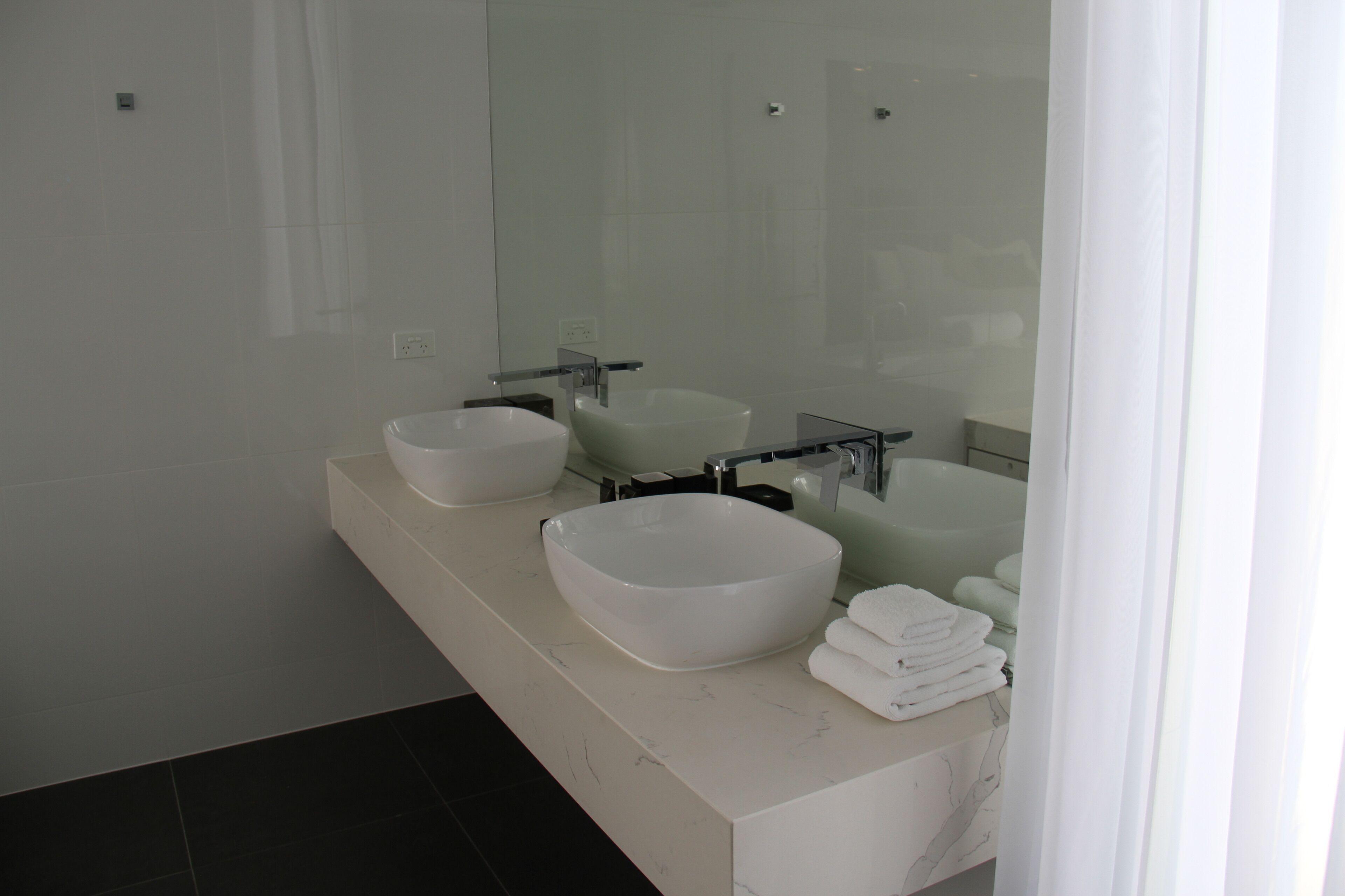 Ein modernes Badezimmer mit zwei großen weißen Waschbecken, einem Spiegel und einem Stapel gefalteter Handtücher.