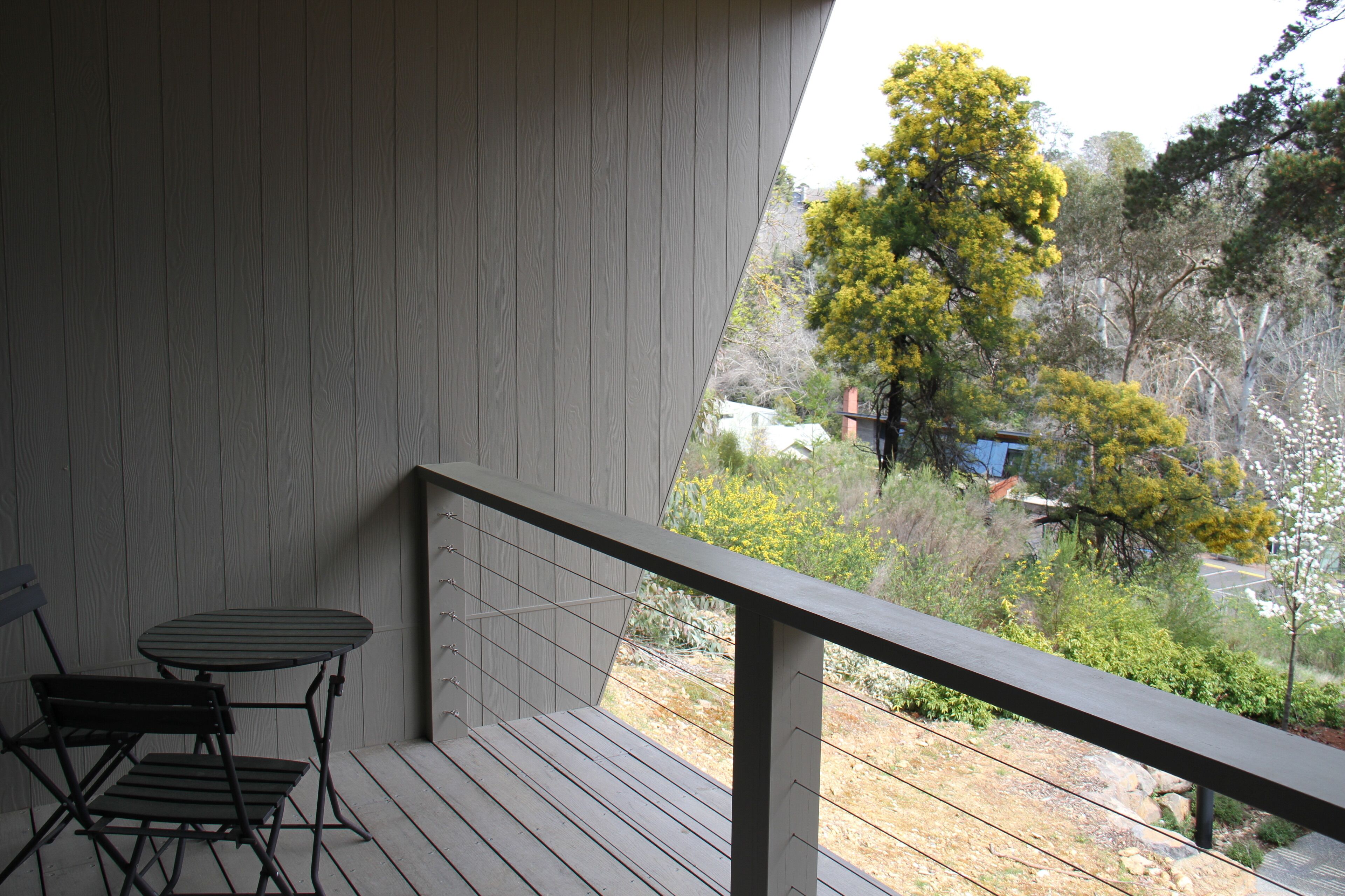 Ein Balkon mit Tisch und Stühlen, der auf einen Garten mit Bäumen und ein Gebäude im Hintergrund blickt.