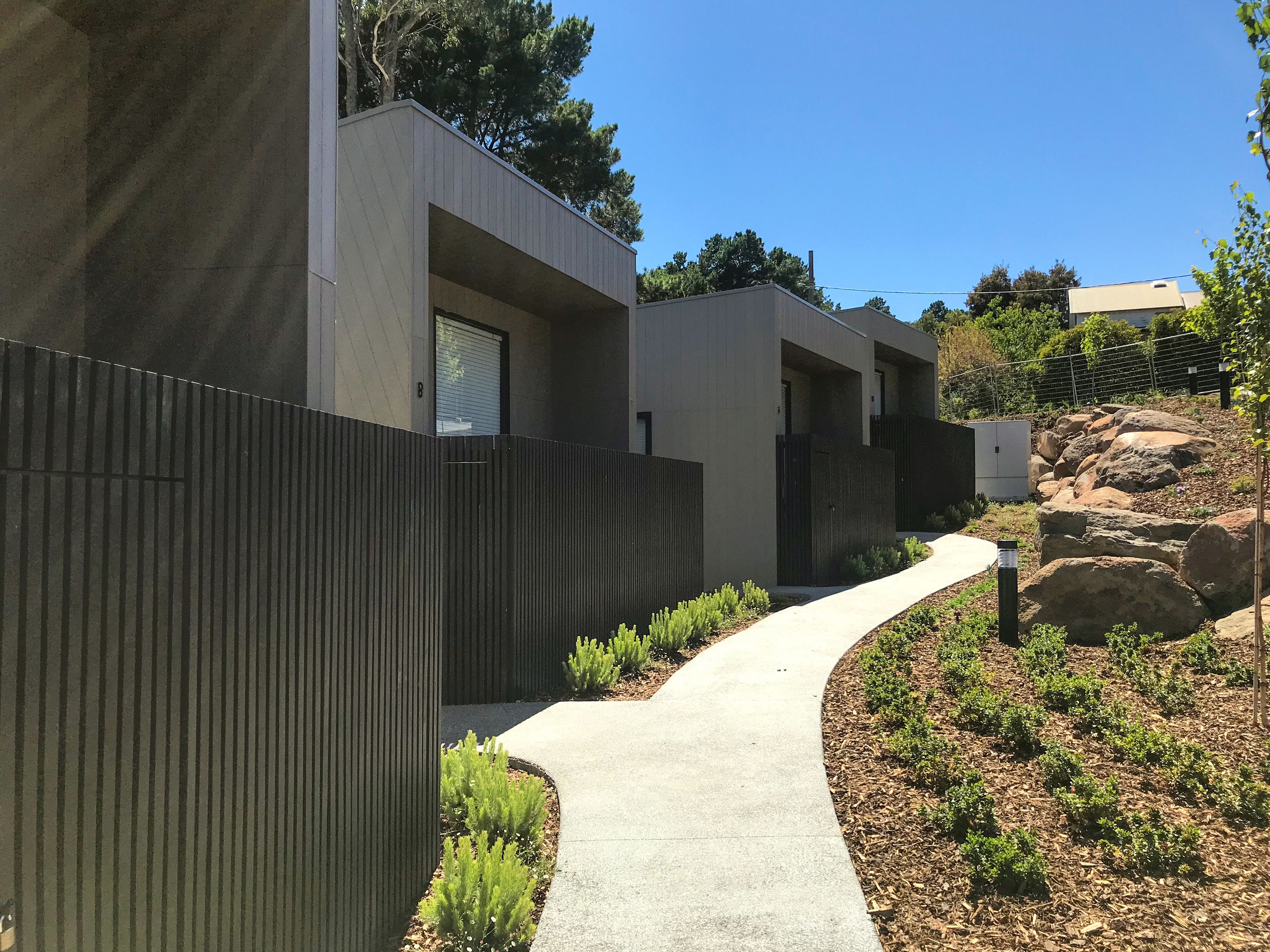 Un bâtiment moderne avec un chemin en béton menant à une entrée fermée par un portail.