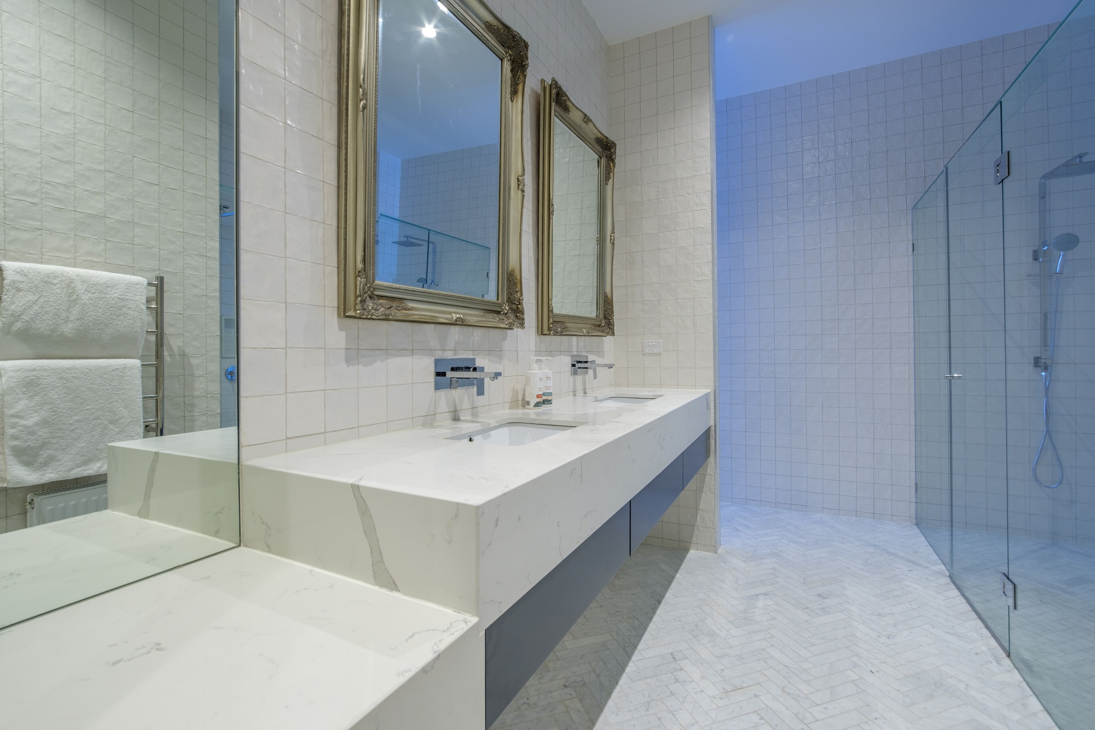 A modern bathroom with a marble vanity, two sinks, a large mirror, and a glass-enclosed shower.