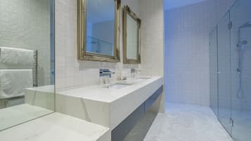 A modern bathroom with a marble vanity, two sinks, a large mirror, and a glass-enclosed shower.