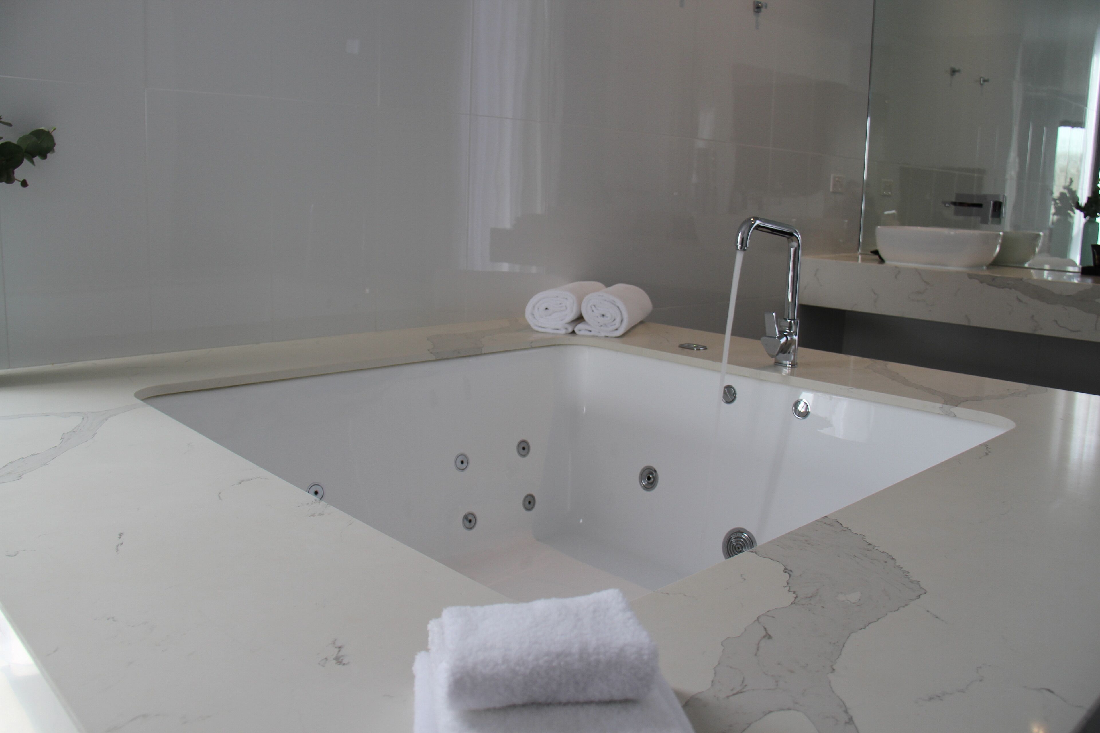A modern bathroom with a large bathtub, a mirror, and two rolled towels on the side.