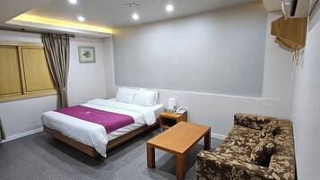 Habitación de hotel con cama, una mesita, un sofá, una ventana y un aire acondicionado de pared.