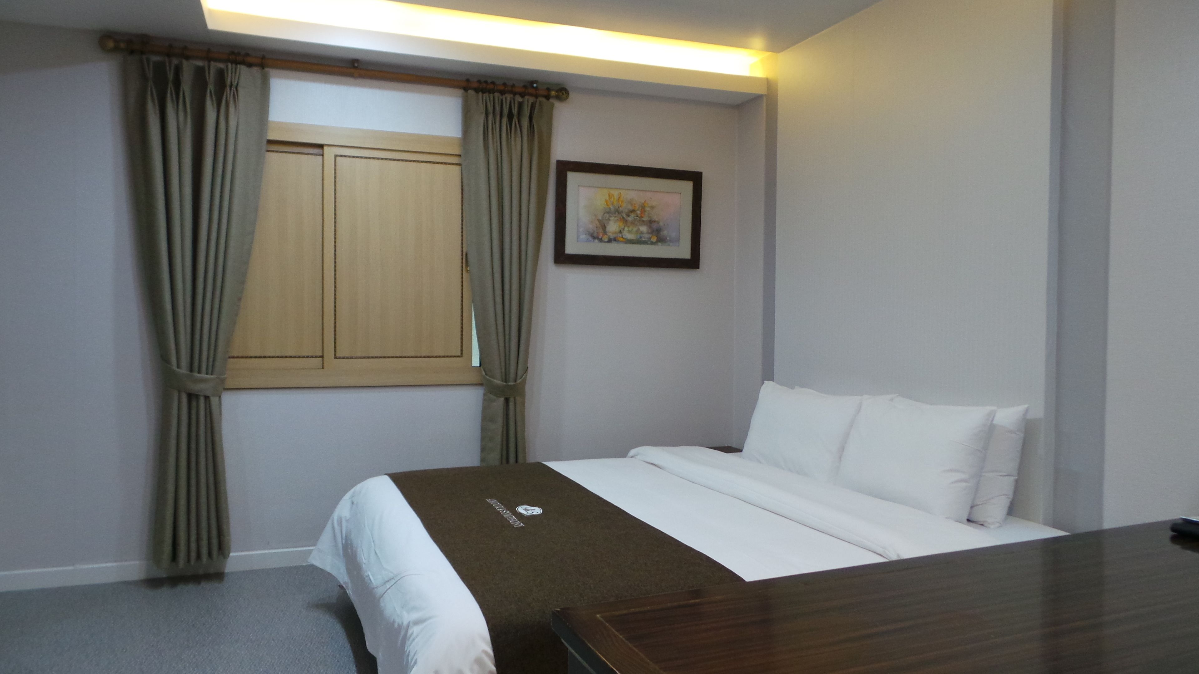 A hotel room with a bed, curtains, a framed picture, and a bedside table.