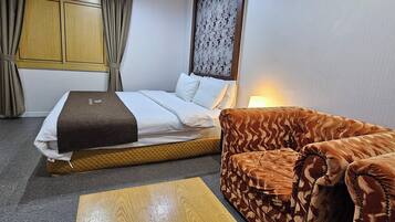 A hotel room with a bed, a sofa, a wooden table, and a patterned wall.