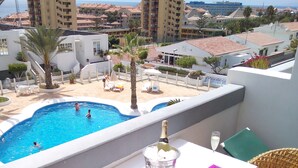 A balcony with a pool, wicker chairs, a table with a bottle of champagne, and a view of the sea and buildings.