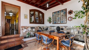 A dining area with a wooden table and wicker chairs, a stone wall with a mosaic, and a staircase leading to an upper level. - Hearth away from house BREIA (Tías)