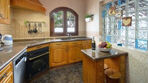A kitchen with wooden cabinets, a built-in oven, a sink, and a window with a view of trees. - Hearth away from house BREIA (Tías)