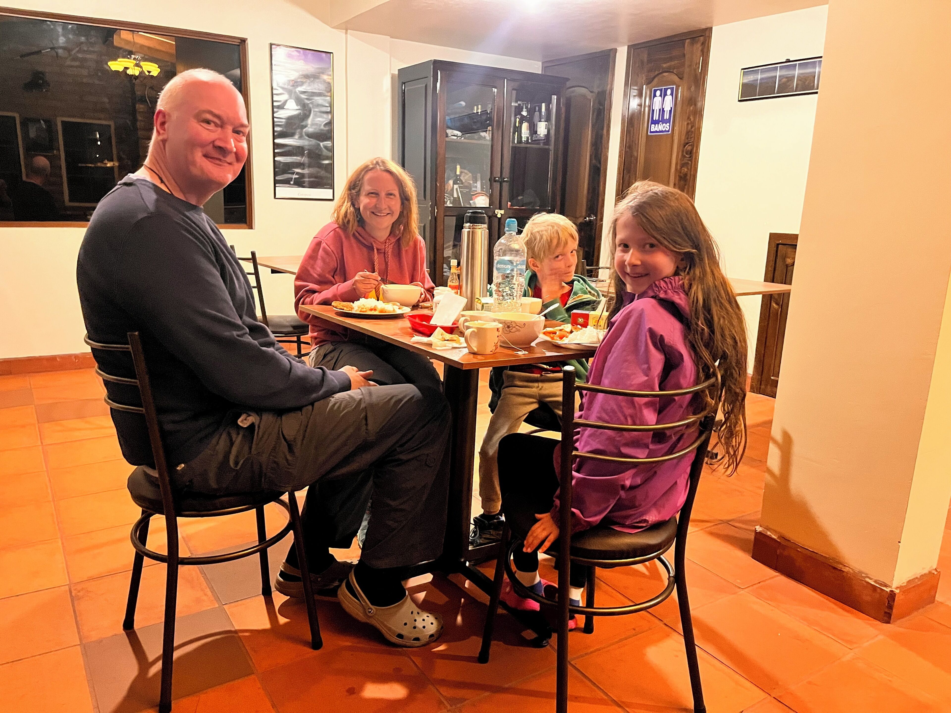 Un comedor con una mesa preparada para cuatro personas, sillas, una ventana y una puerta con un cartel.