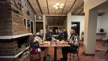 Eine Gruppe von Personen speist an einem Holztisch in einem Raum mit Kamin aus Stein und Holzbalkendecke.