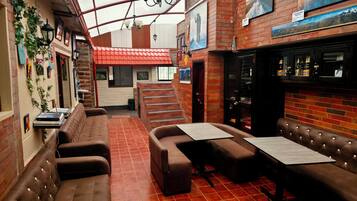 Un interior acogedor con pared de ladrillo, suelo de baldosas rojas y una zona de estar con mesas y bancos acolchados.