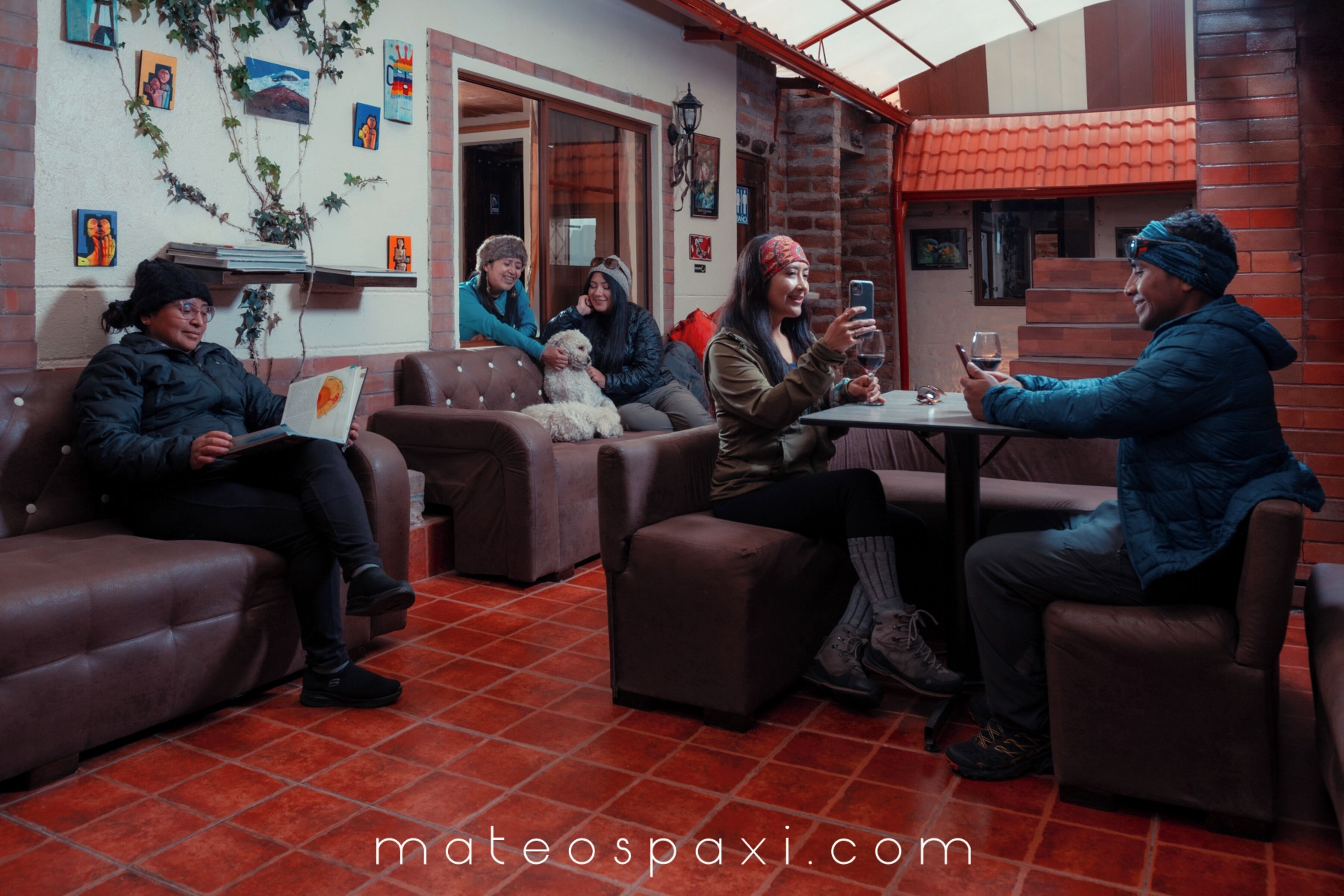 A group of people sitting on leather couches and chairs in a cozy outdoor setting with a tiled floor and brick walls.