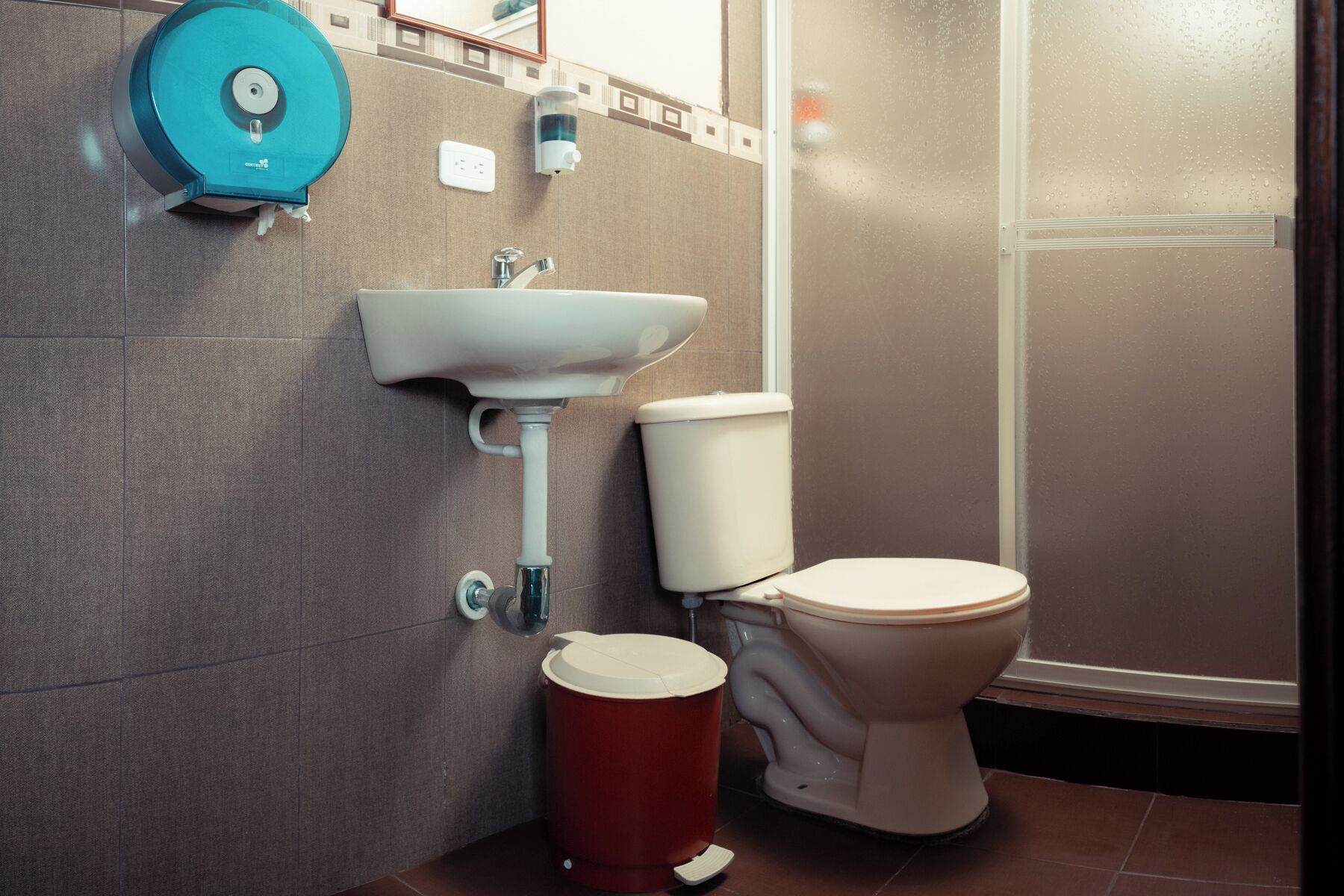 A bathroom with a sink, toilet, and a red trash bin.