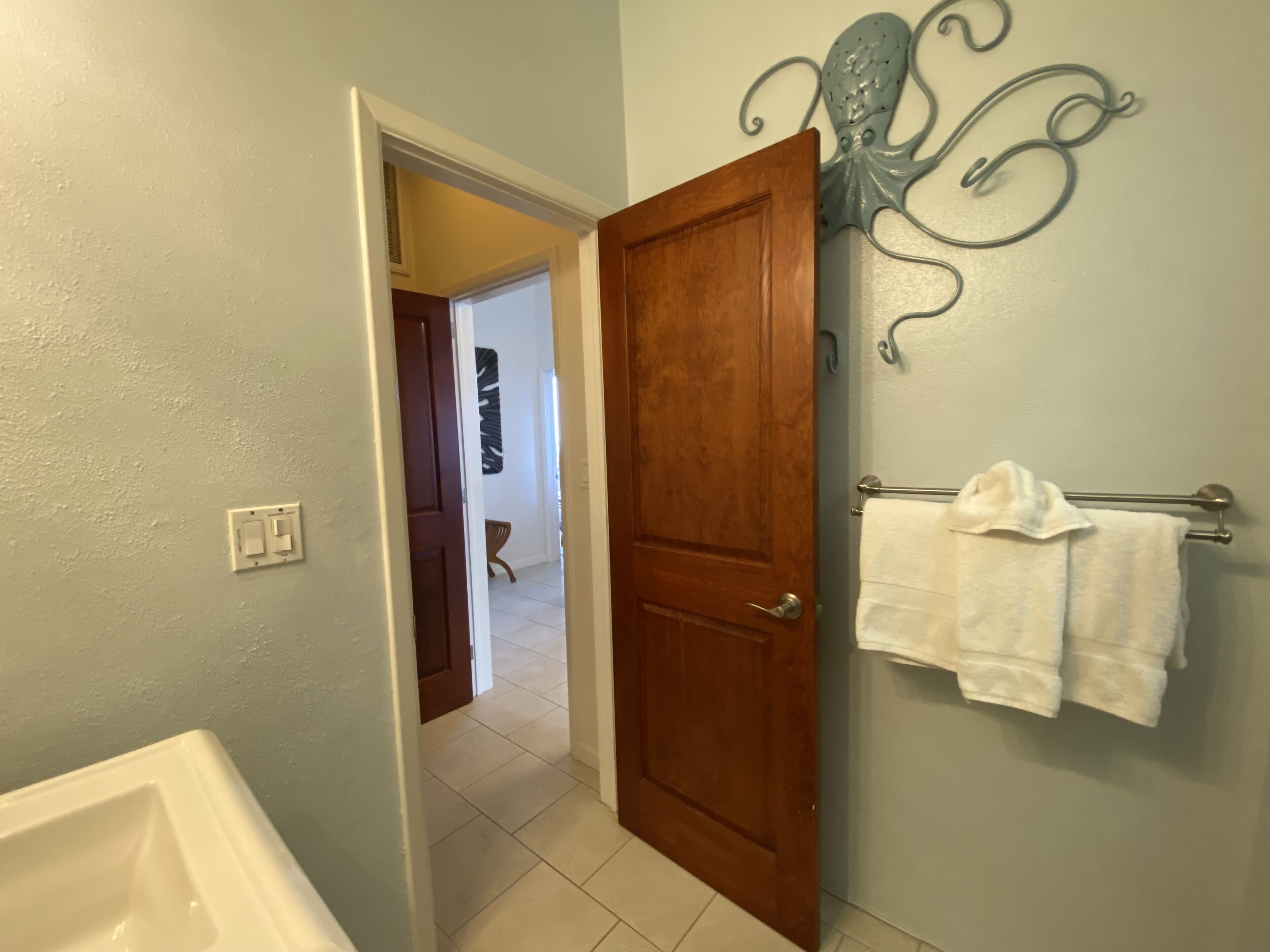 Casa de banho com porta de madeira, um porta-toalhas com toalha branca e um objeto decorativo fixado na parede.