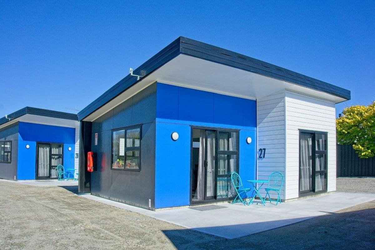 A modern building with a blue and white exterior, numbered 27, featuring large windows and a small patio area with chairs.