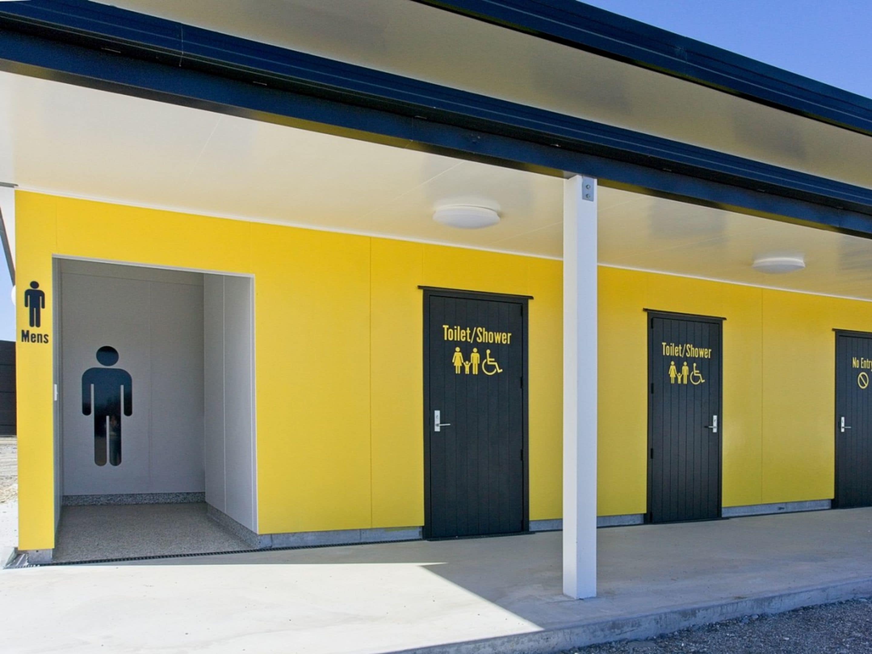 A building with yellow walls and black doors, each marked with symbols for men, women, and disabled access.