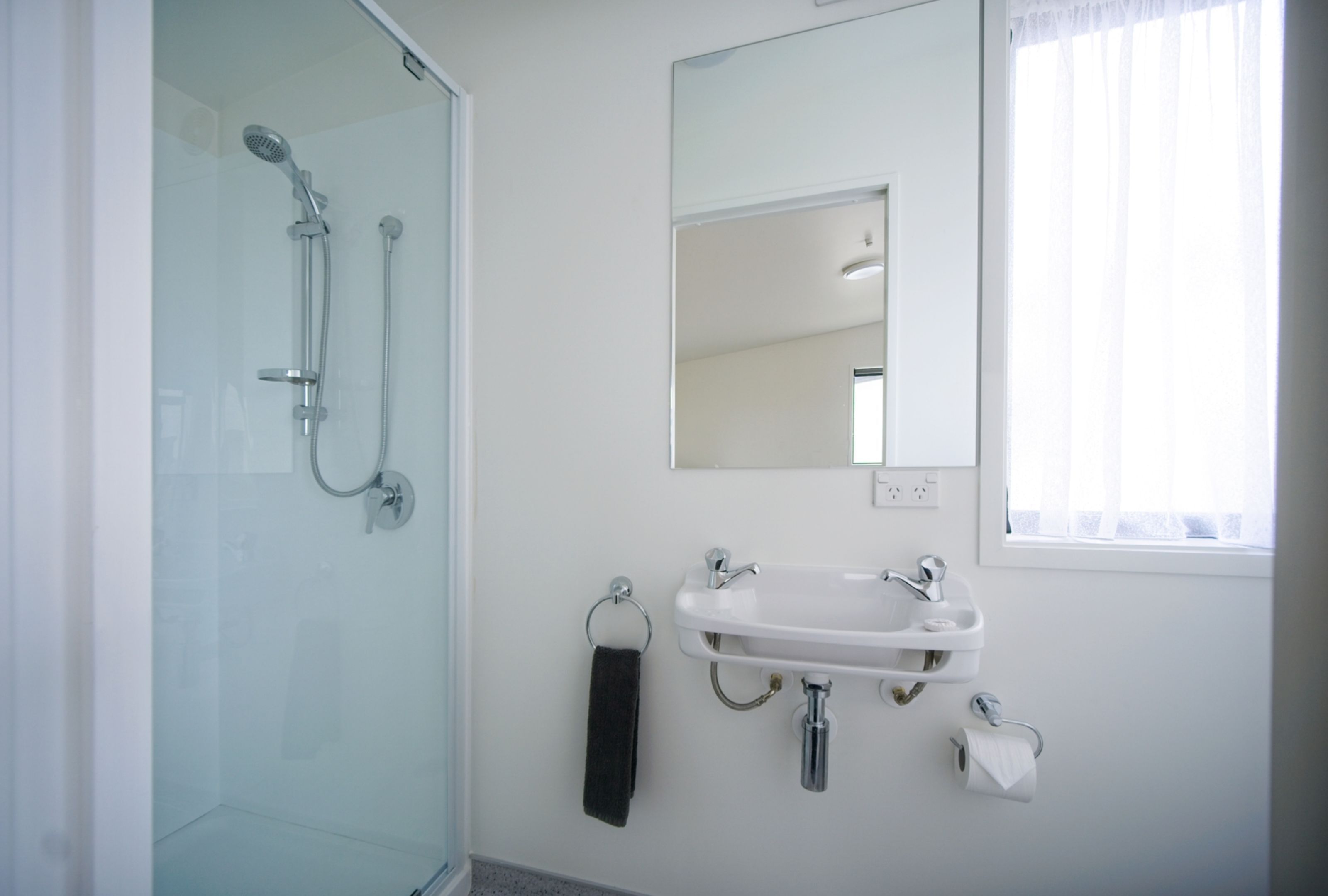 A bathroom with a glass shower enclosure, a white sink, a mirror, and a window with curtains.