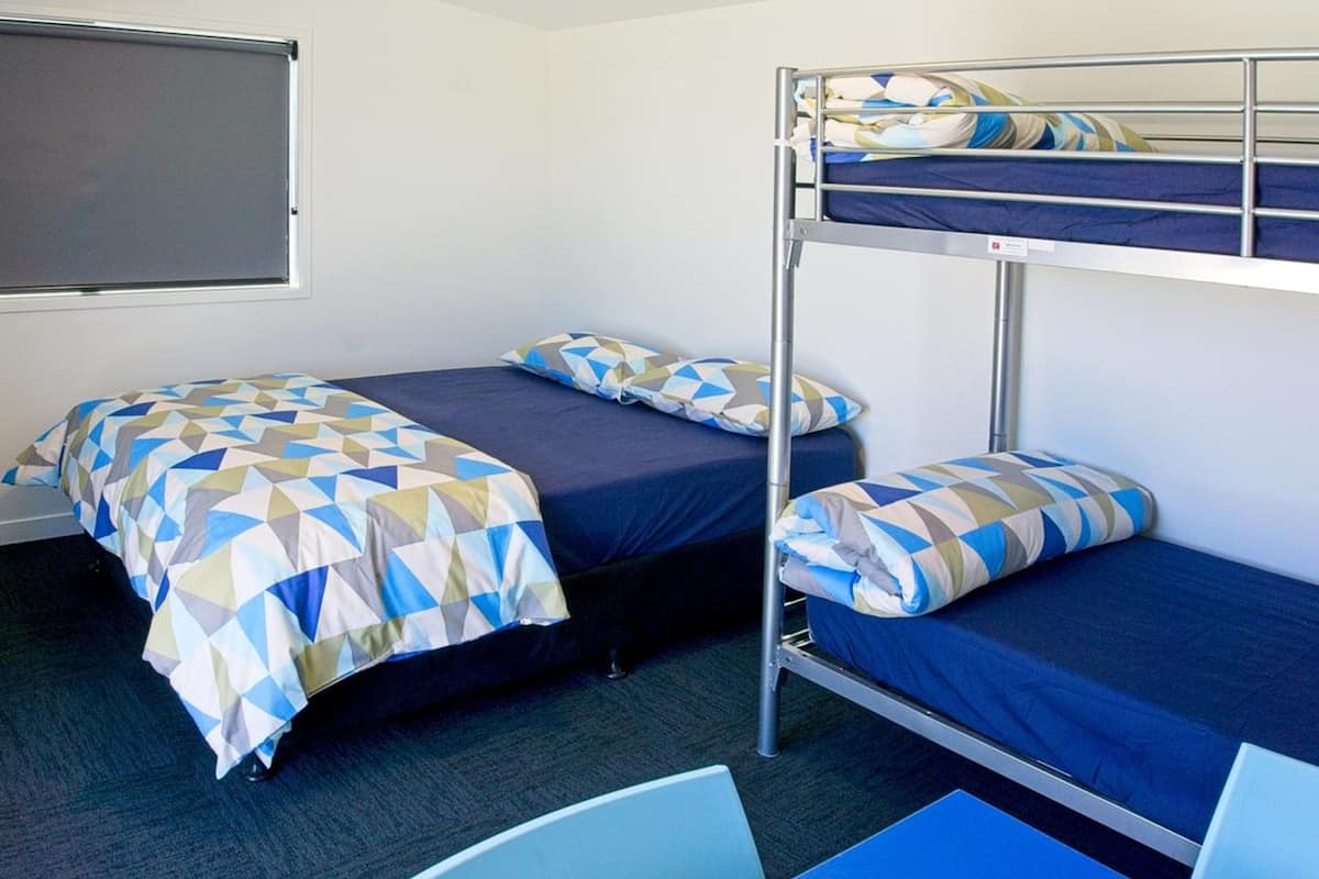 A dormitory room with bunk beds, a desk, and a chair.