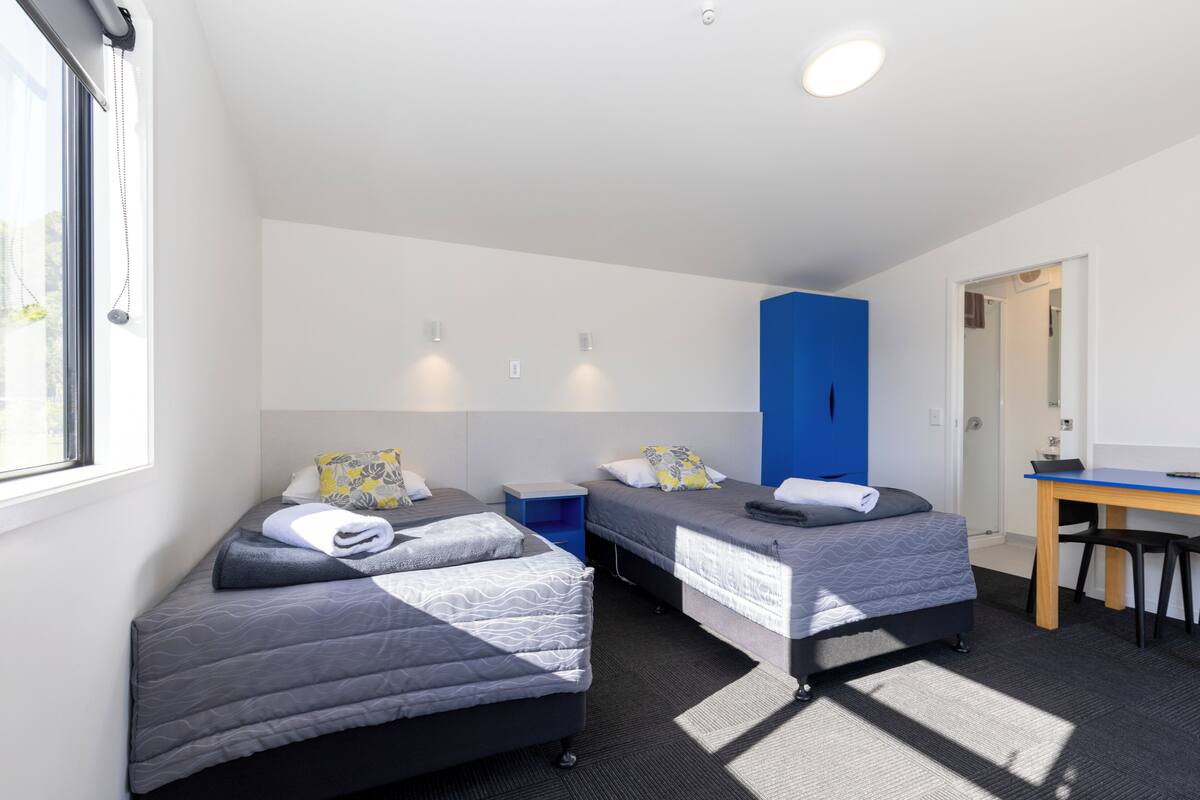 A room with two single beds, a desk, and a blue wardrobe.