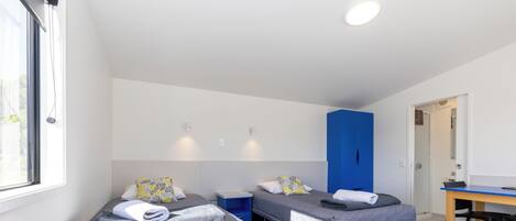 Een kamer met twee eenpersoonsbedden, een bureau en een blauwe garderobe.