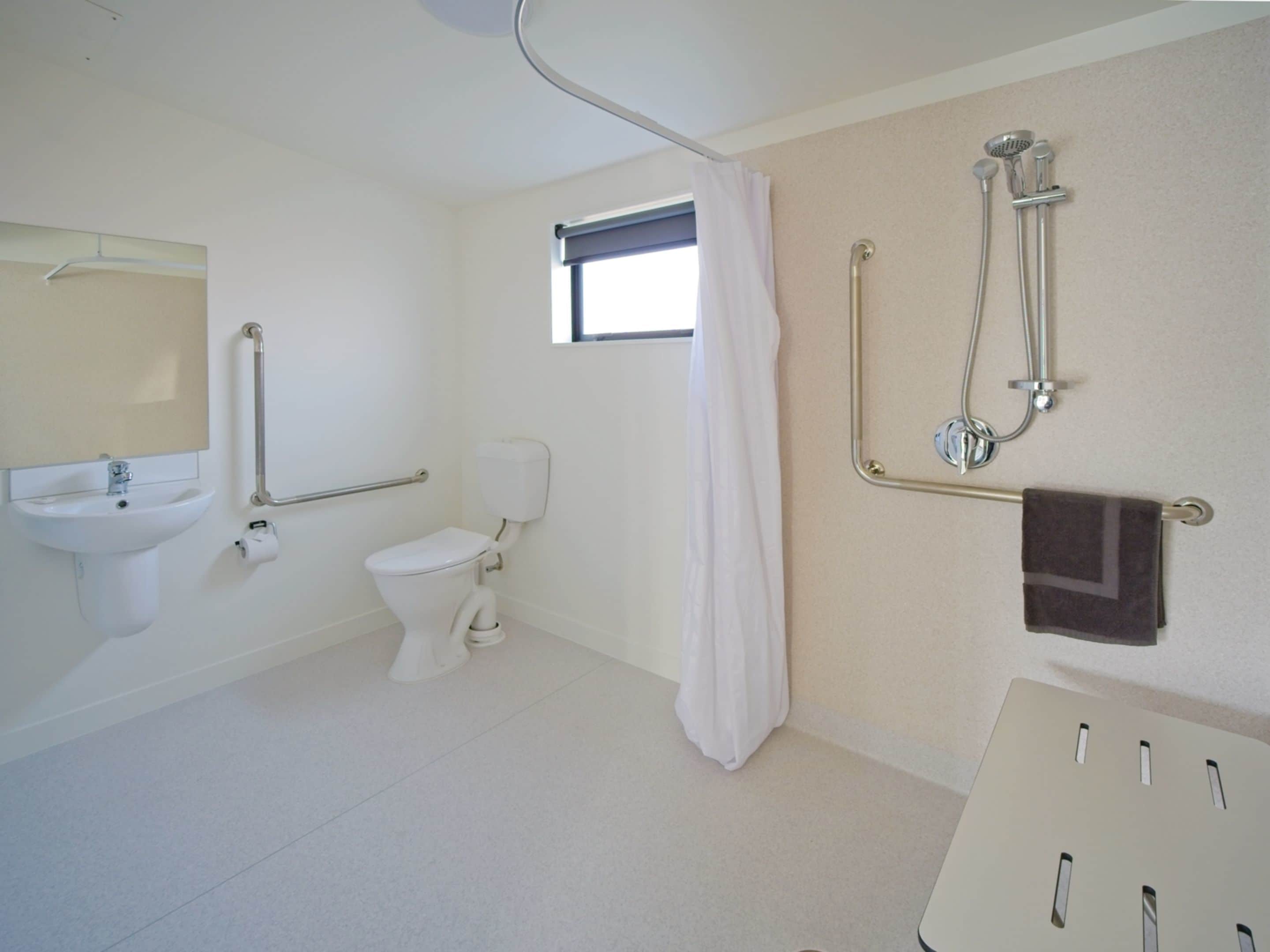 A bathroom with a toilet, sink, shower, and grab bars.
