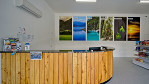 A reception desk with a wooden finish, a white wall with framed photos of landscapes, and a white shelf with various items.