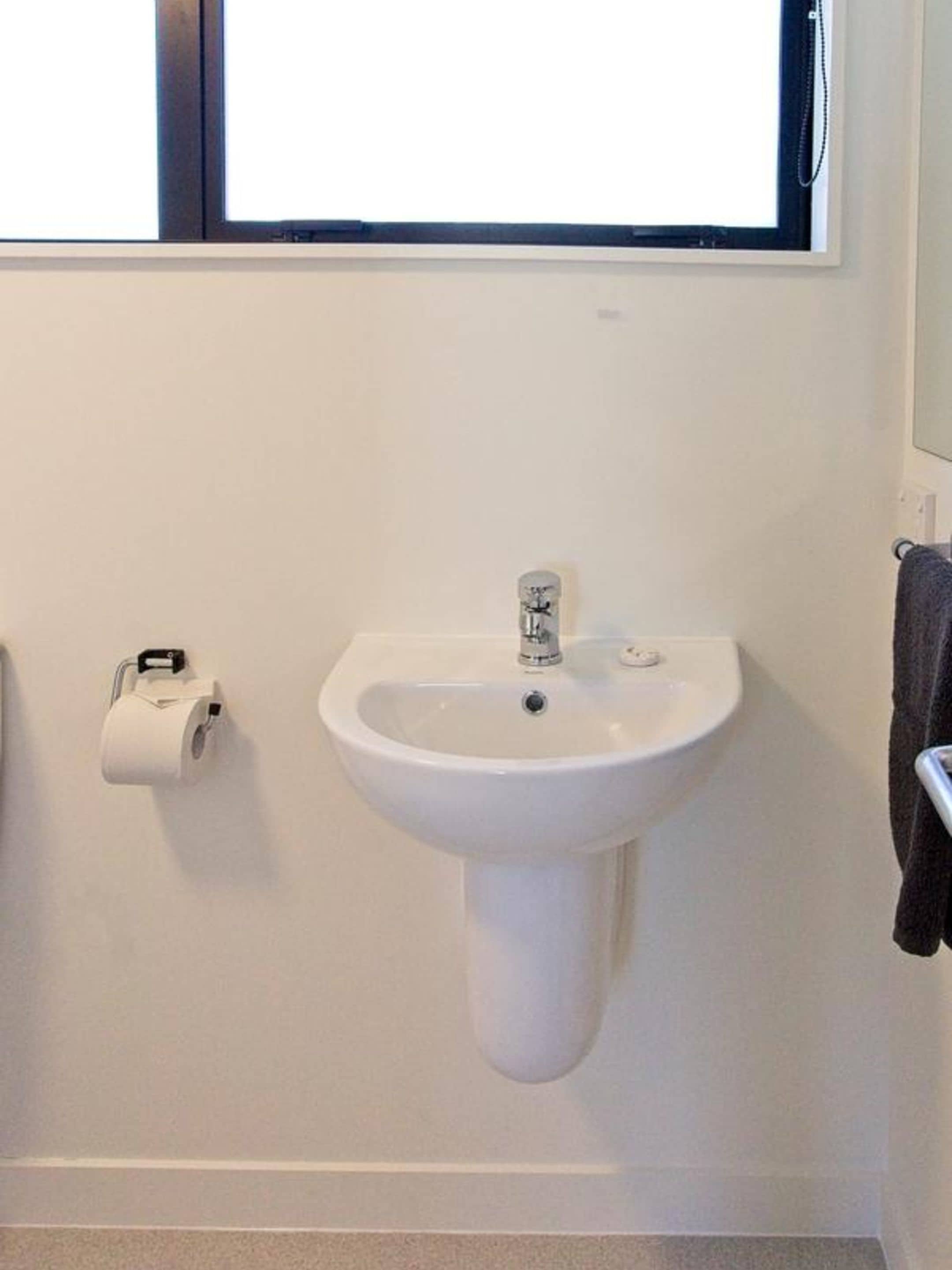 Een badkamer met een witte wastafel, een toiletrolhouder en een handdoekrek.
