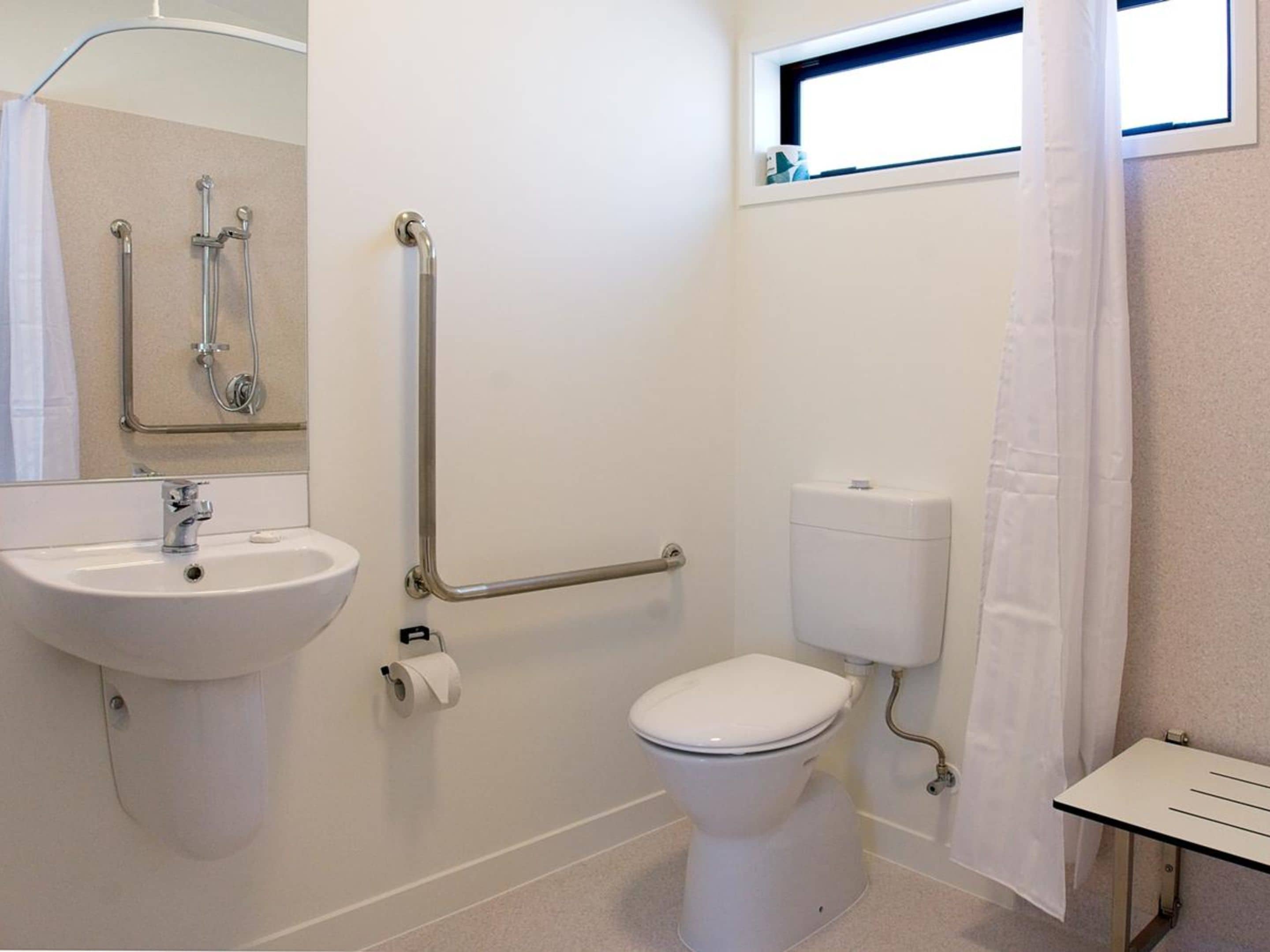 Un baño con lavamanos, inodoro y barras de apoyo.