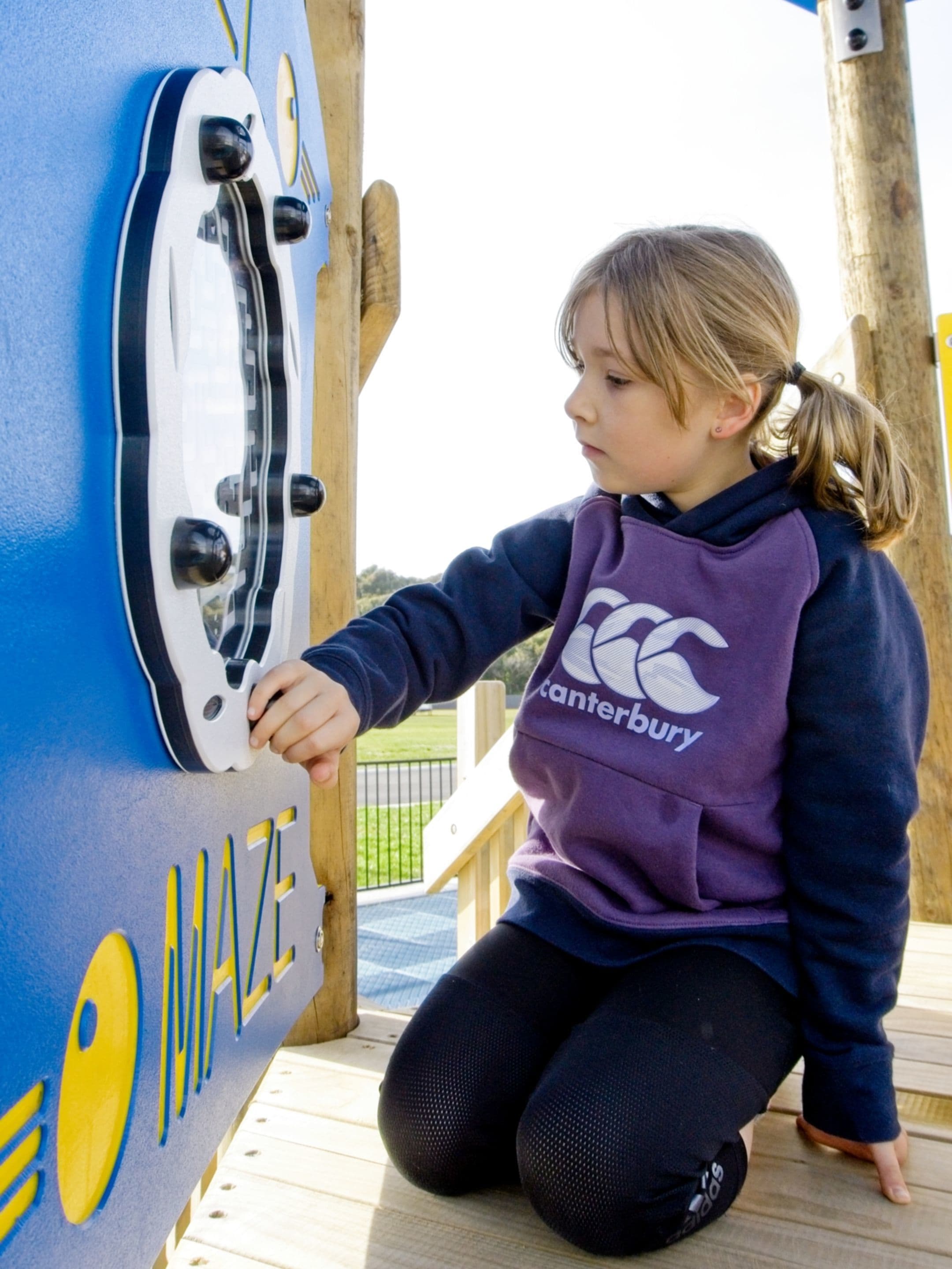 A child interacting with a large, colorful play structure labeled "Maze" on a wooden deck.