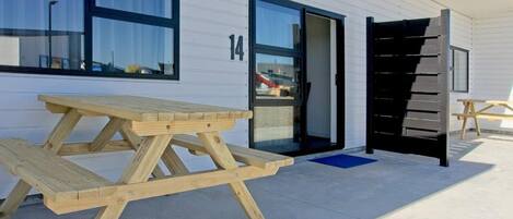 A wooden picnic table outside a building with a number '14' on the wall.