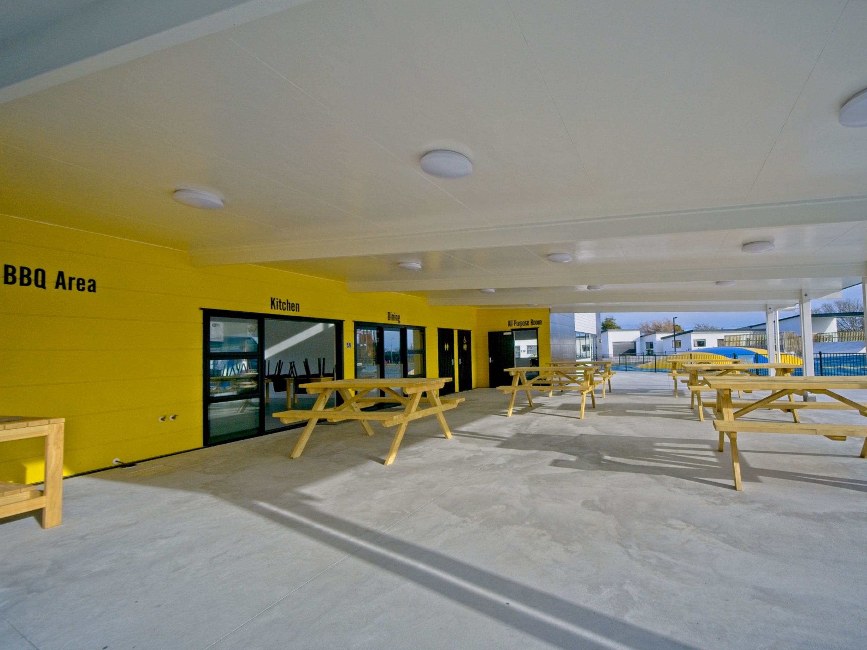 An outdoor area with a BBQ section, a kitchen, dining area, and an all-purpose room.