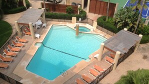 A rectangular swimming pool with a diving board, surrounded by lounge chairs and a fence.