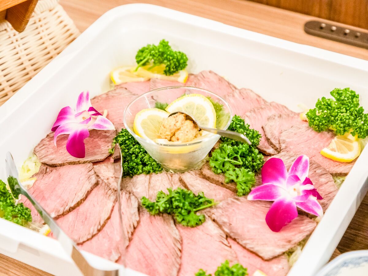 Una bandeja de carne en rodajas adornada con perejil, rodajas de limón y flores.