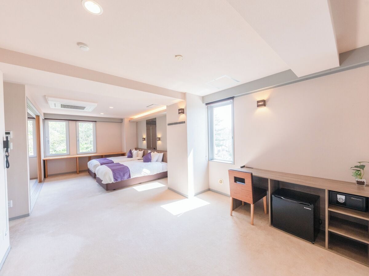 Un dormitorio moderno con cama, mesitas de noche, escritorio y un mini refrigerador empotrado.
