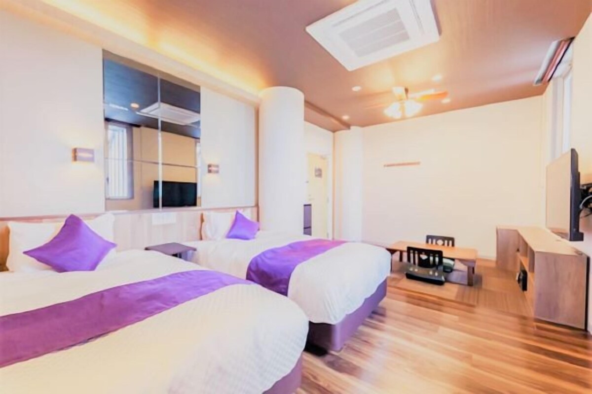 A hotel room with two beds, a desk, and a television.