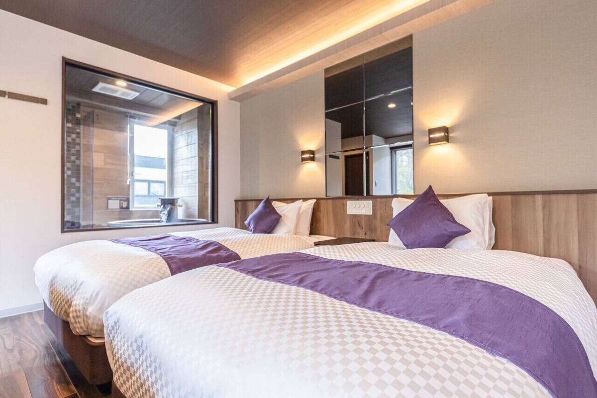 A hotel room with two beds, a large window, and a mirror above the beds.