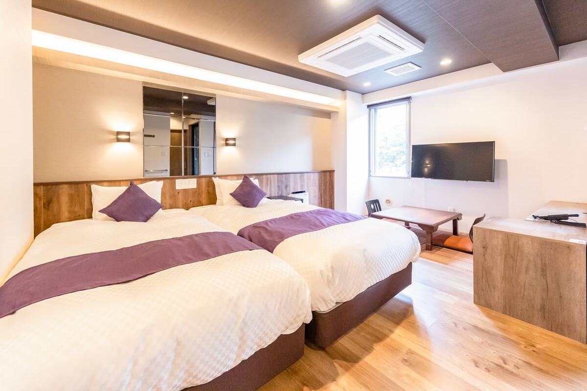 A modern hotel room with two beds, a desk, and a TV.