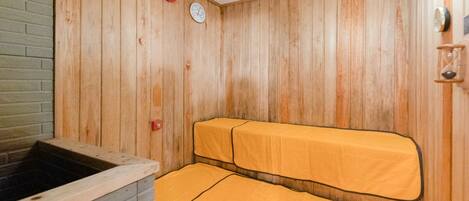 A sauna room with wooden walls, a bench, and a hot tub.