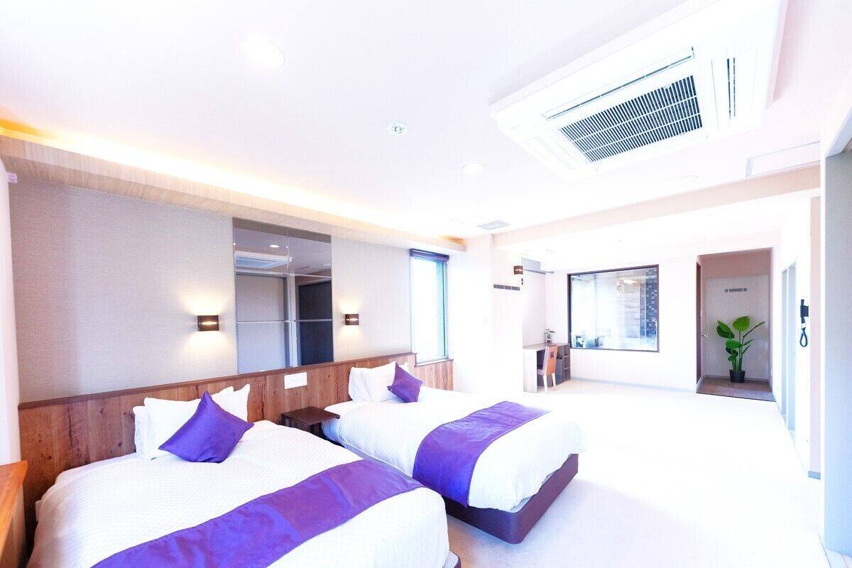 A hotel room with two beds, a large mirror, and a view of the hallway.